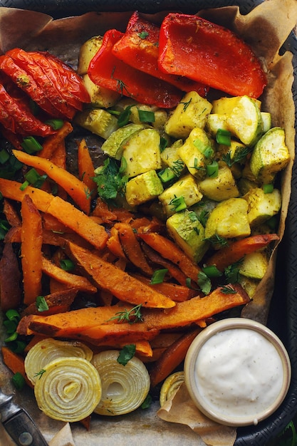 Batatas caseras al horno con tomates, cebollas, pimiento rojo y salsa sobre fondo rústico, concepto de alimentación saludable, vista superior