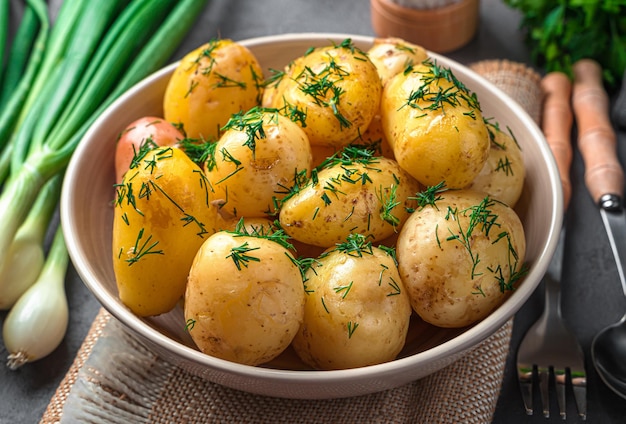 Batatas com casca jovens cozidas frescas com endro e manteiga em um fundo escuro com endro e especiarias