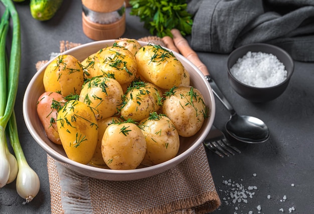 Batatas com casca jovens cozidas frescas com endro e manteiga em um fundo escuro com endro e especiarias