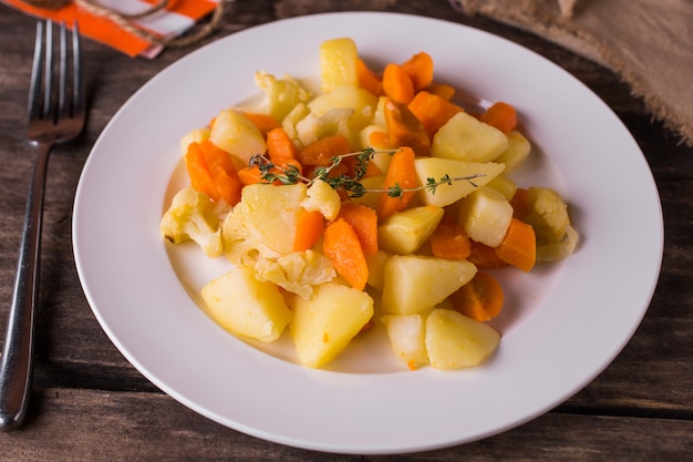 Batatas cozidas com legumes e cenouras no prato branco na mesa de madeira rústica