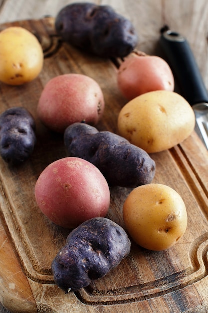 Batatas cruas com descascador de legumes em uma placa de madeira