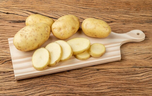 Batatas cruas com fatias em uma tábua sobre a mesa de madeira.