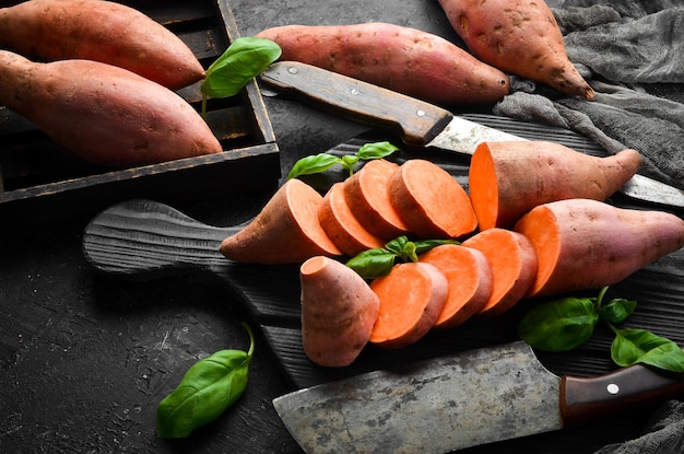 Foto batatas crudas y albahaca sobre un fondo de piedra negra. vista superior. espacio libre para su texto.