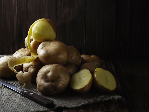 Batatas descascadas com uma faca na mesa foto em uma chave escura