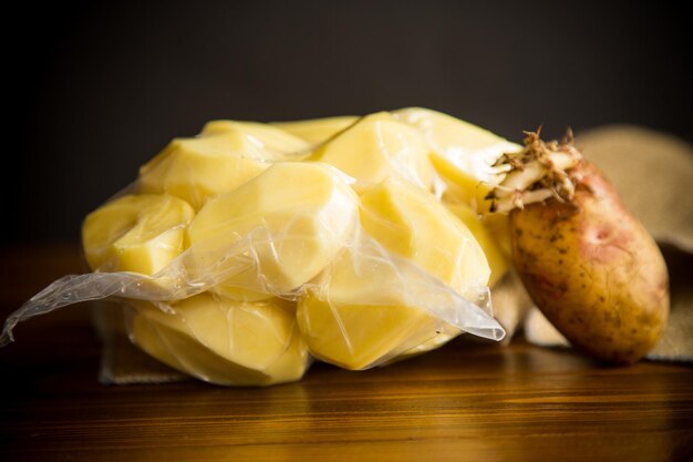 batatas descascadas fechadas em um saco de vácuo e batatas velhas germinadas em uma mesa de madeira