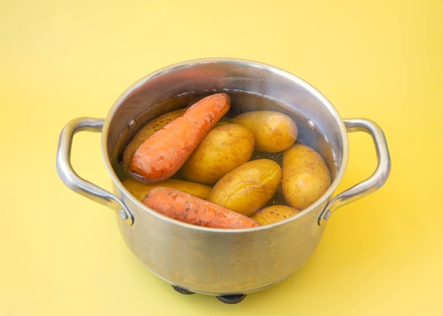 Batatas e cenouras de legumes cozidas em uma panela em um fundo amarelo