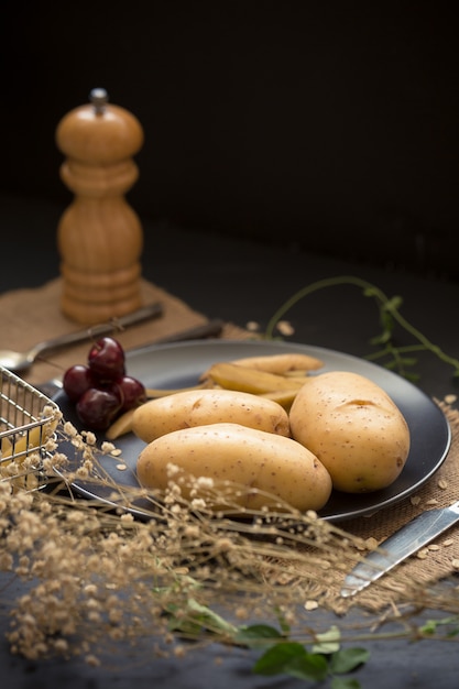 Batatas e frutas cereja na placa preta em pano de saco e mesa de madeira escura