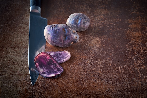 Batatas fatiadas de vitelotte, três fatias na faca e duas batatas inteiras no escuro