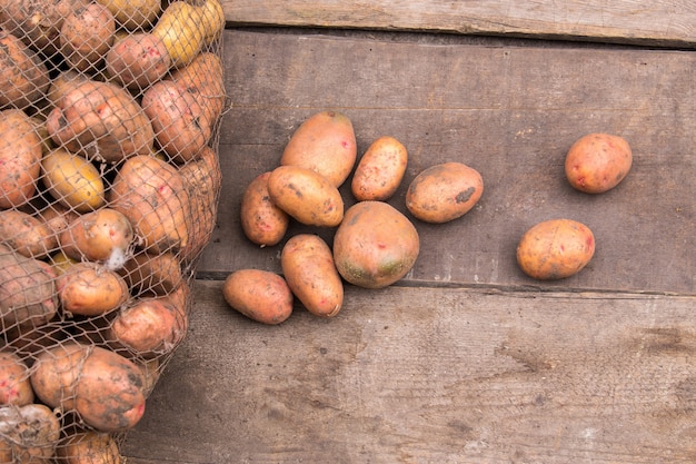 Batatas frescas colhidas com o solo ainda na pele, saindo de um saco de estopa, em uma paleta de madeira áspera.