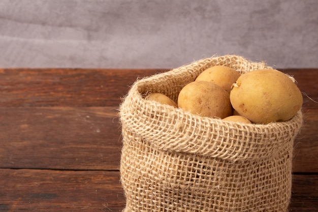 Batatas frescas e cruas em um saco rústico na mesa de madeira