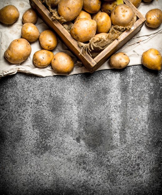 Batatas frescas em uma velha caixa de madeira. Na mesa rústica.