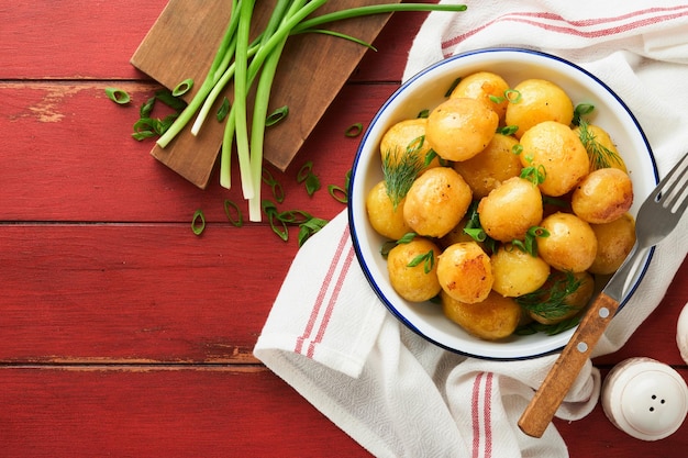 Batatas frescas ou jovens cozidas com manteiga, endro e cebolas frescas em tigela branca sobre um fundo de madeira rústico vermelho velho, batatas cozidas novas e saborosas.