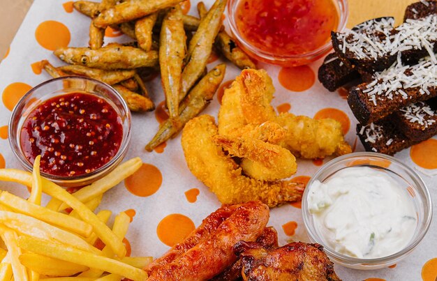 Foto batatas fritas batatas com anéis de cebola salsichas croutons e pernas de frango picantes