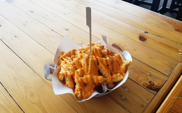 Batatas fritas cobertas com queijo servidas em uma tigela colocada sobre uma mesa de madeira