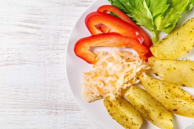 Foto batatas fritas com chucrute, pimentão e aipo em um prato branco.