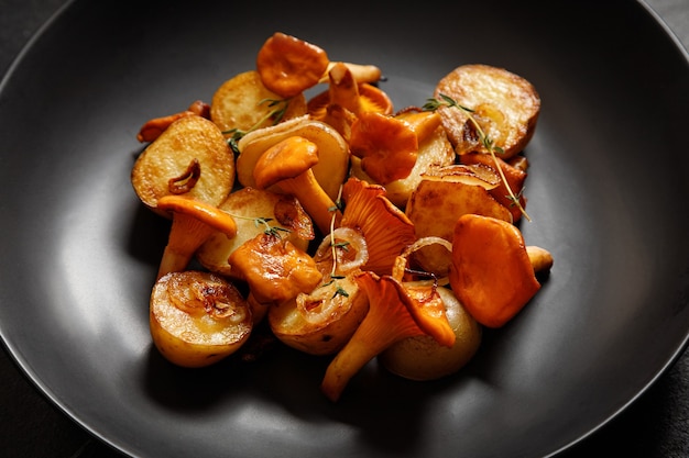 Batatas fritas com cogumelos chanterelles em um prato preto sobre um fundo preto para o jantar