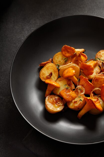 Batatas fritas com cogumelos chanterelles em um prato preto sobre um fundo preto para o jantar