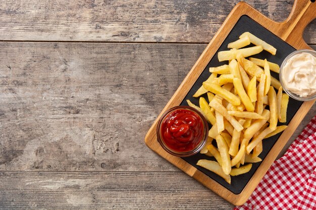 Batatas fritas com ketchup e maionese na mesa de madeira