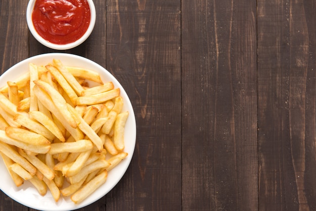 Batatas fritas com ketchup em fundo de madeira