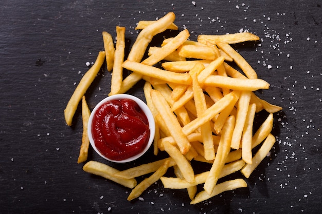 Batatas fritas com ketchup em fundo escuro