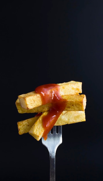 Batatas fritas com ketchup picadas em um garfo no fundo preto Closeup Location vertical