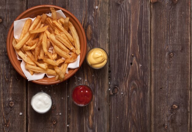 Batatas fritas com molho na mesa de madeira.