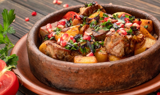 Foto batatas fritas com sementes de carne e romã, em um prato de barro, sobre um fundo de madeira com ervas e tomate