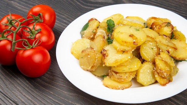 Batatas fritas cozidas com ervas e vegetais em um prato branco sobre uma mesa de madeira