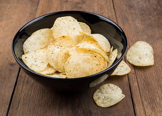 Batatas fritas crocantes em tigela preta em estilos vintage de fundo de mesa de madeira velha