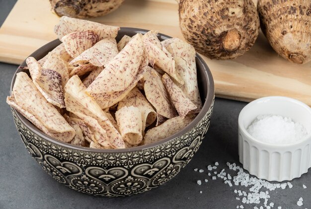 Batatas fritas de inhame ou taro em uma tigela com vegetais crus sobre a mesa de madeira.