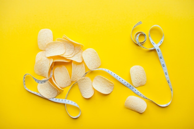 Batatas fritas e fita métrica em um fundo amarelo brilhante para perda de peso e conceito de dieta