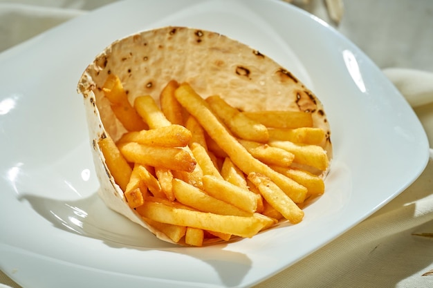 Batatas fritas em um prato branco de toalha de mesa branca Luz dura Foco seletivo Closeup