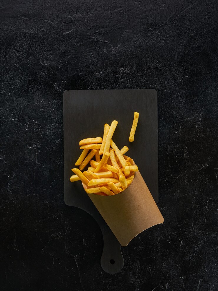 Foto batatas fritas em uma caixa de papel artesanal na placa de madeira, vista superior com espaço de cópia