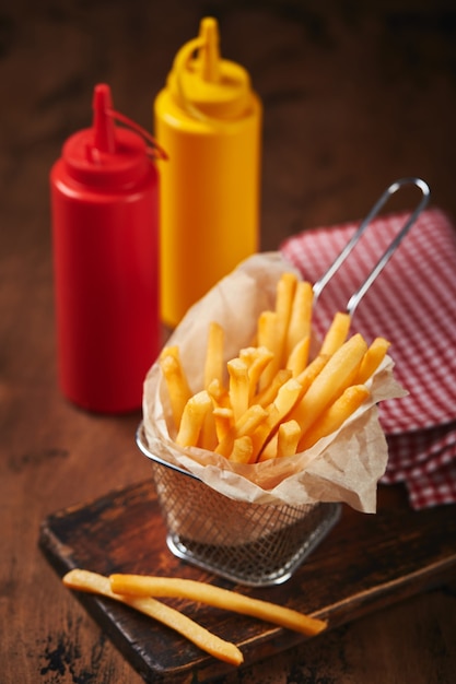 Batatas fritas em uma cesta de malha de metal em uma placa de madeira conceito de fast food comida americana