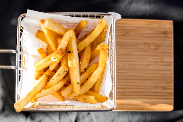 Batatas fritas em uma cesta de metal em um assoalho de madeira.