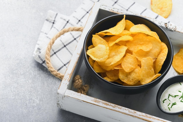 Batatas fritas Fast food Batatas fritas crocantes tigela preta cerâmica com molho de creme de leite e cebolas em carrinho de madeira na mesa de cozinha cinza fundo de concreto Tradição americana Hot BBQ Vista superior