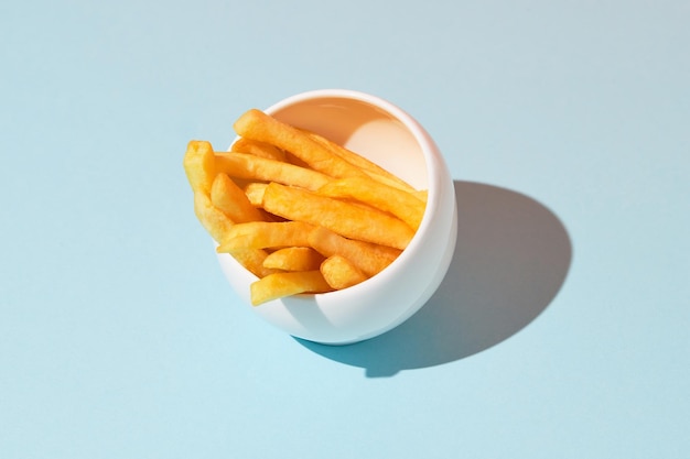 Batatas fritas frescas e saborosas em prato sobre fundo azul, sombras longas e profundas da moda