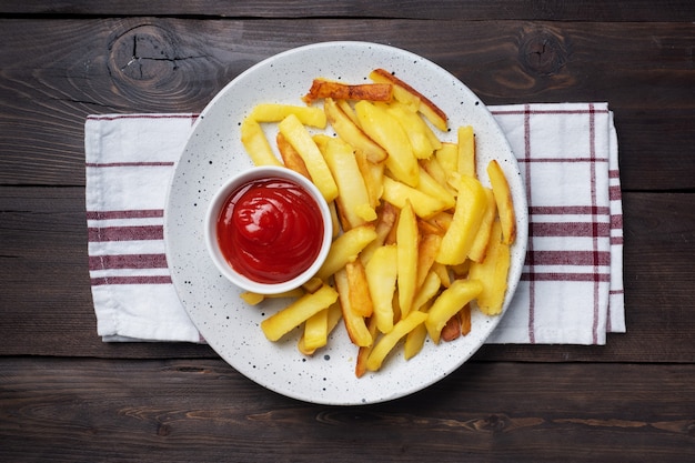 Batatas fritas fritas com molho de ketchup de tomate em um prato. mesa de madeira. Copie o espaço.