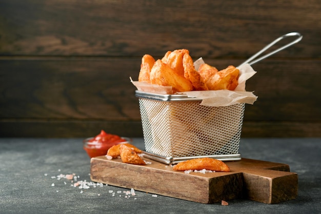 Batatas fritas na cesta de arame de metal com sal e ketchup no velho fundo escuro de madeira clous Up Batatas fritas Fast-food e conceito de comida pouco saudável