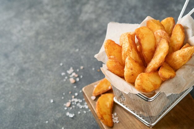 Batatas fritas na cesta de arame de metal com sal e ketchup no velho fundo escuro de madeira clous Up Batatas fritas Fast-food e conceito de comida pouco saudável