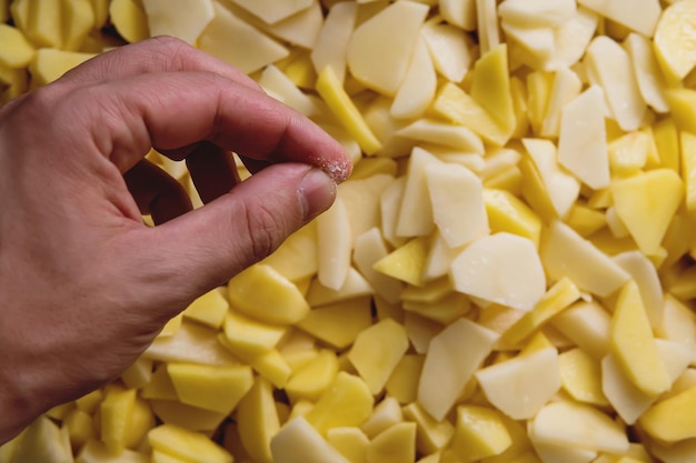 Batatas fritas polvilhadas com sal em um balde de ferro As batatas frescas salgadas à mão Cozinhar pratos de batata Mãos salgadas