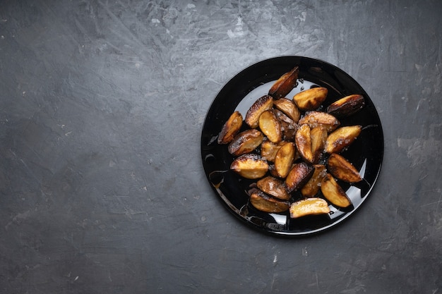 Batatas fritas rústicas em um prato preto na mesa, vista de cima