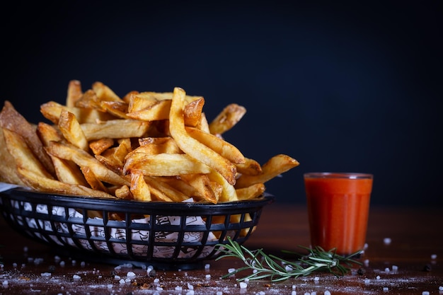 Foto batatas fritas servidas em uma tábua de corte de cesta em uma mesa de madeira preta batatas frites rústicas feitas à mão