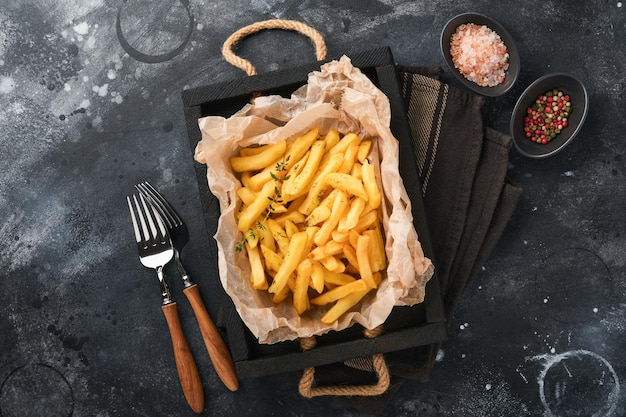 Batatas fritas Servidor de batatas fritas saborosas em papel pergaminho na tábua de madeira com molho de tomate e queijo em fundo preto velho Diversos pratos Keto Fast food e conceito de comida insalubre