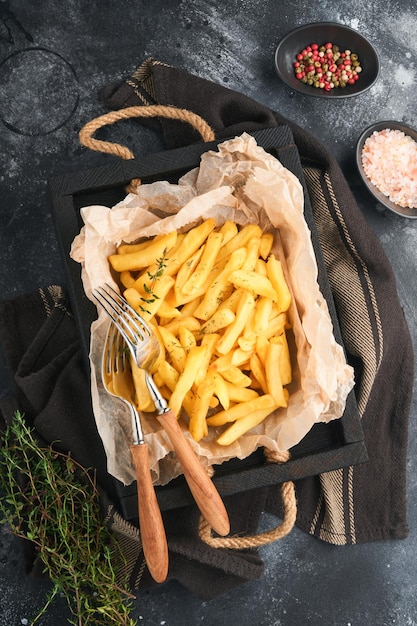 Batatas fritas Servidor de batatas fritas saborosas em papel pergaminho na tábua de madeira com molho de tomate e queijo em fundo preto velho Diversos pratos Keto Fast food e conceito de comida insalubre