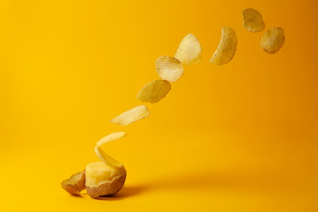 Foto batatas fritas voam sobre um fundo amarelo o processo de fazer chips de levitação de fast food