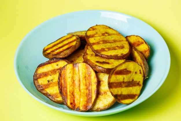 Foto batatas grelhadas até dourarem em um prato azul sobre fundo amarelo