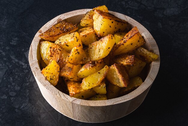 Batatas grelhadas em uma tigela de madeira na superfície preta