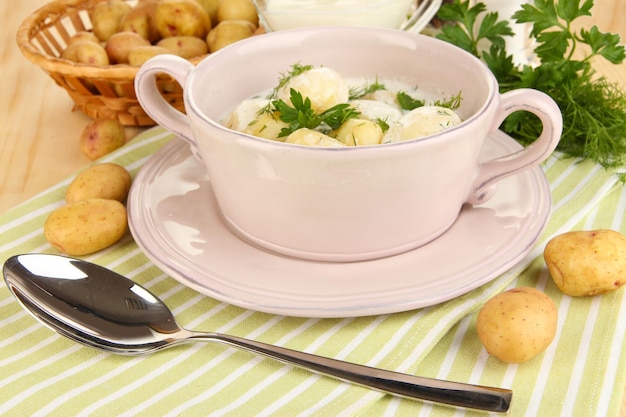 Batatas tenras com creme de leite e ervas na panela na mesa de madeira fechada