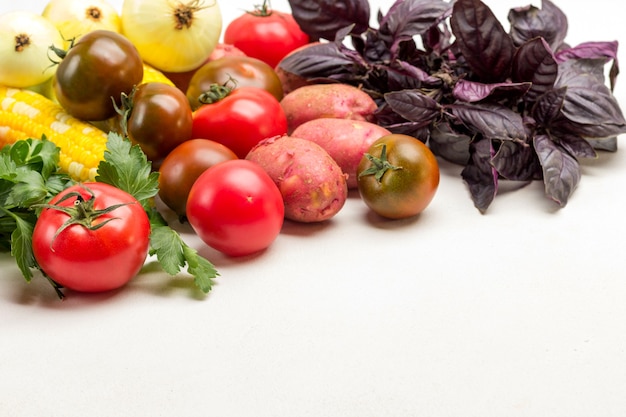 Batatas, tomates, cebola e raminhos de basi azul no branco. Conjunto de vegetais na mesa. Copie o espaço. Postura plana